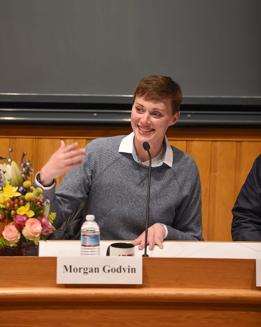 Morgan Godvin speaking on a panel at Harvard University, a 'Morgan Godvin' nameplate on the table in front of her